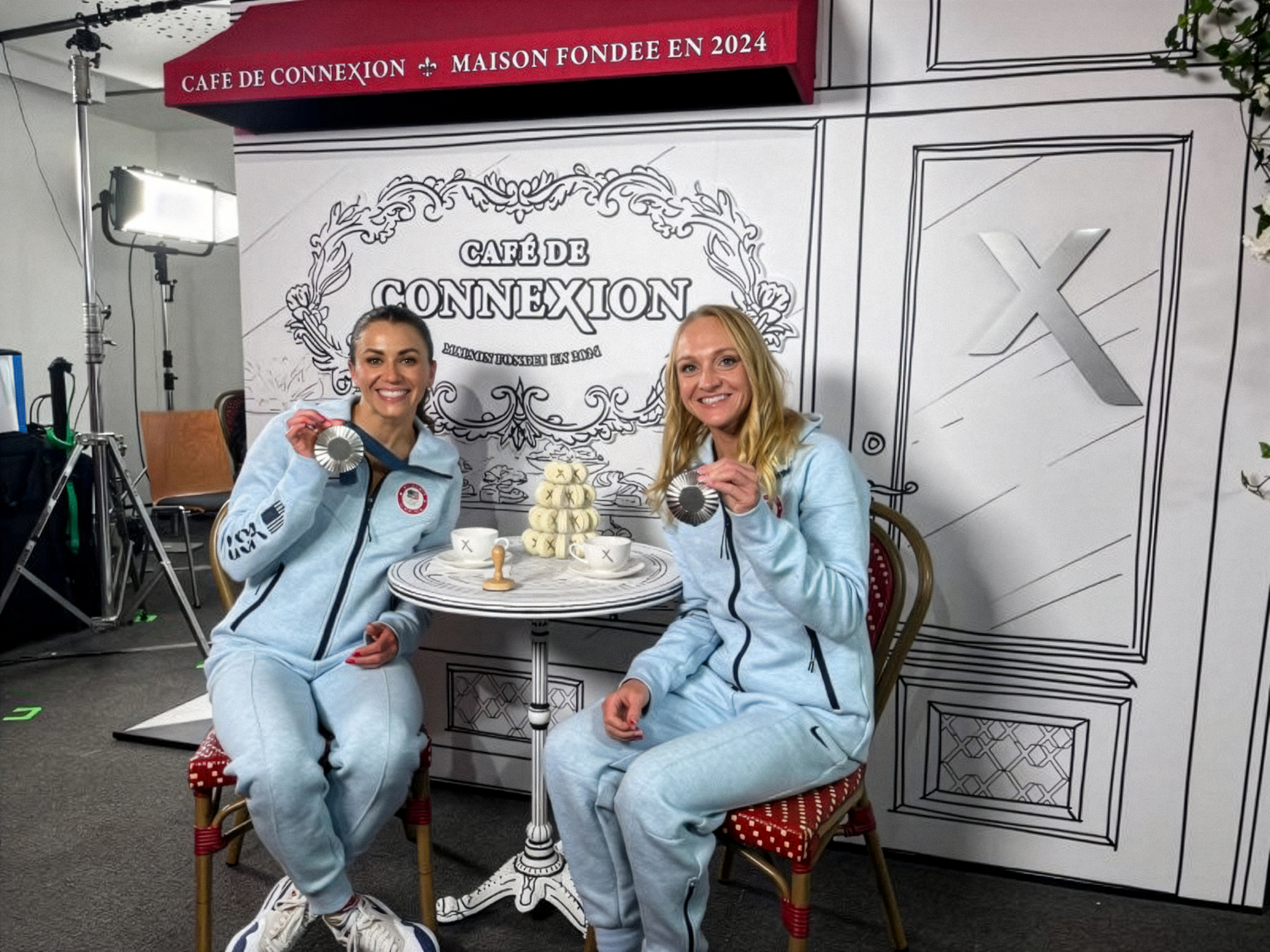 Two Team USA athletes displaying their medals at the Xfinity Connections Cafe.